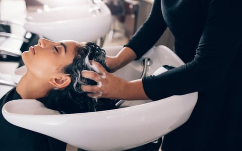 Woman getting hair washed at salon sink by stylist with shampoo and water
