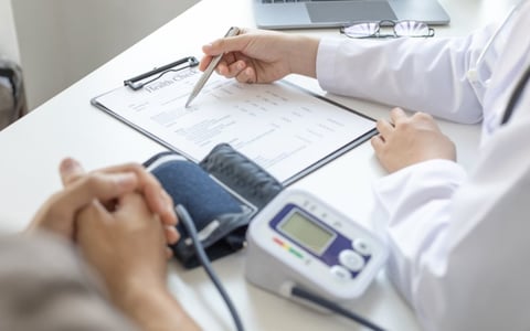 Doctor reviewing blood pressure test results with patient, consulting medical chart at desk